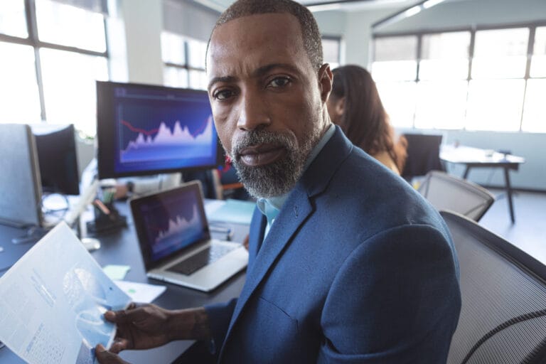 Person sat at a desk working on computer with graphs and charts whilst looking towards camera.