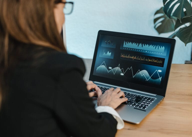 Looking over shoulder of a woman working on a laptop looking at charts and graphs.