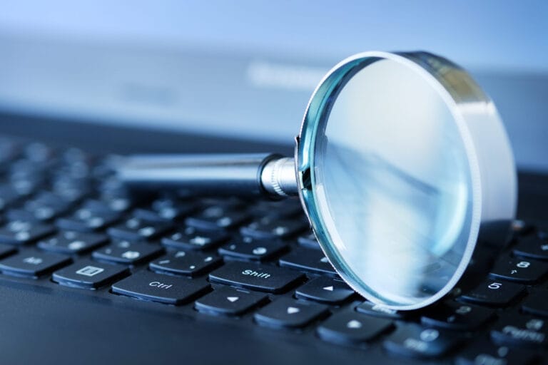 Magnifying glass balanced on top of a laptop keyboard.