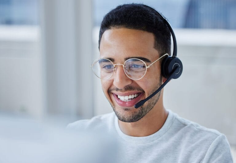 Smiling customer support agent wearing headset sat in front of a computer screen.