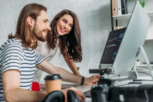 Selective focus of happy art editor looking at computer monitor near coworker.