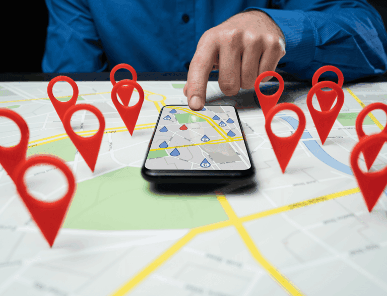 Person pointing at phone laid on a map with pin locations hovering.
