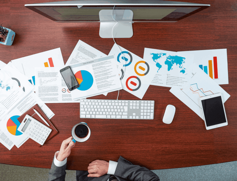 Business person sat at wooden office desk with reports laid out in front of them.